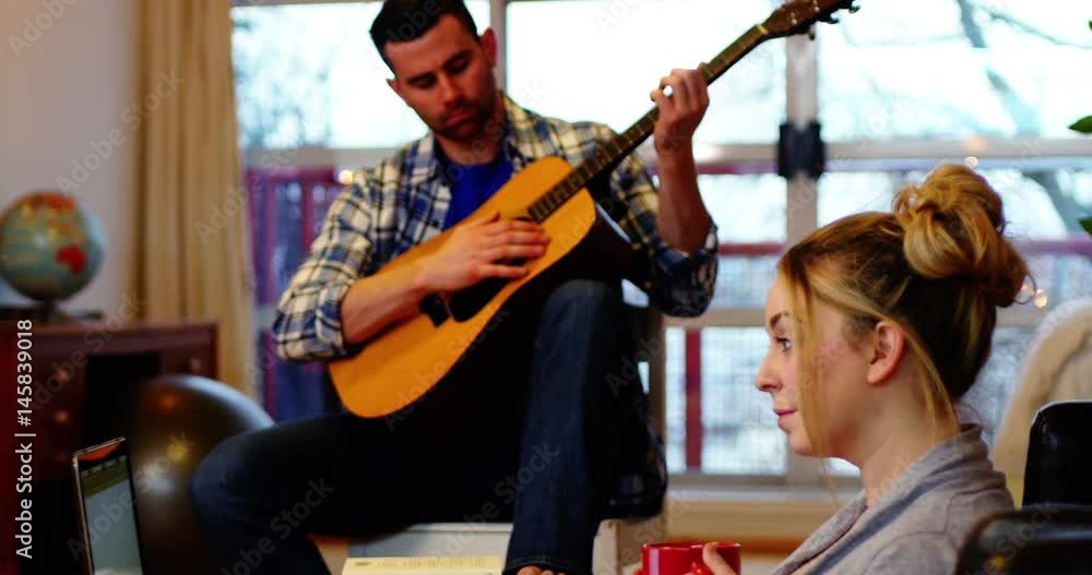 Man playing guitar while woman using laptop Man playing guitar while woman using laptop