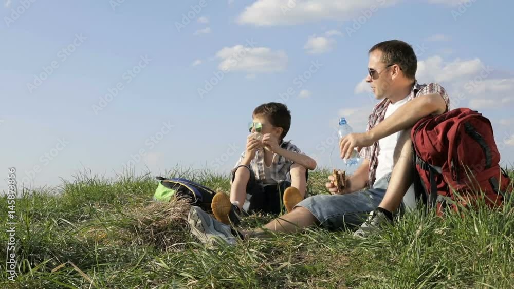 Father and son sitting in the field at the day time. People having fun outdoors. Concept of friendly family. Father and son sitting in the field at the day time. People having fun outdoors. Concept of friendly family.