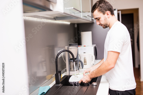 Fotografie young happy man doing the dishes smiling confident and relaxed enjoying doing do