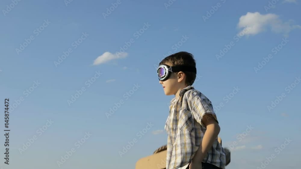 Little boy playing with cardboard toy airplane in the park at the day time. Concept of happy game. Child having fun outdoors. Picture made on the background of blue sky. Little boy playing with cardboard toy airplane in the park at the day time. Concept of happy game. Child having fun outdoors. Picture made on the background of blue sky.