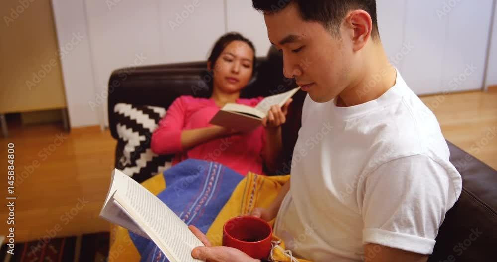 Couple relaxing on sofa reading book in living room Couple relaxing on sofa reading book in living room