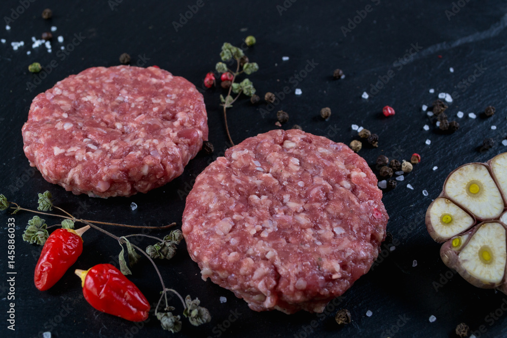 Fresh raw meat burger cutlet on the black slate board with herbs and spices for background. Copy space, top view . Selective focus. Fresh raw meat burger cutlet on the black slate board with herbs and spices for background. Copy space, top view . Selective focus.