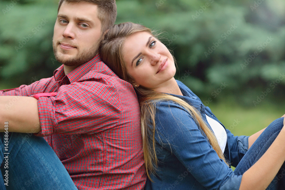 Young adult couple siting back in back in nature Young adult couple siting back in back in nature