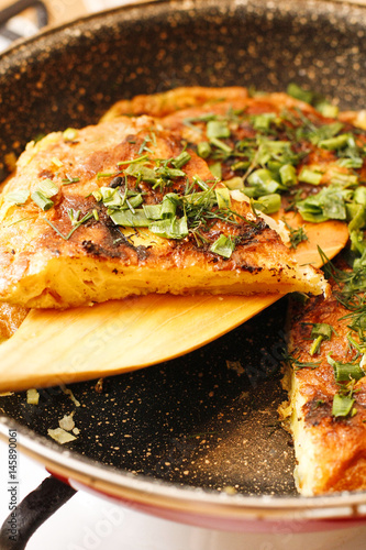 Stodgy Spanish potato tortilla with herbs in black pan