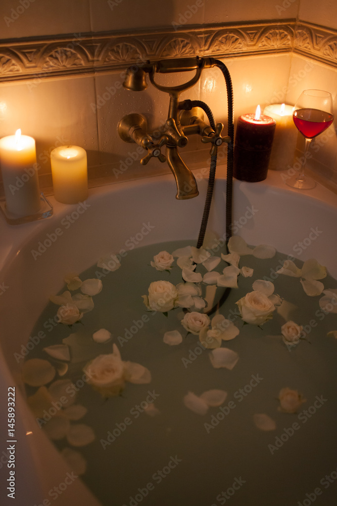 Take a bath with rose petals and candles. Romantic evening in the bathroom with wine and candles