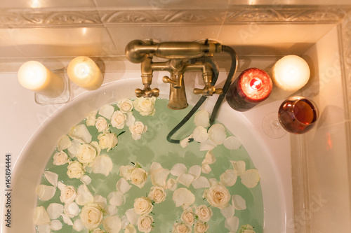 Take a bath with rose petals and candles. Romantic evening in the bathroom with wine and candles