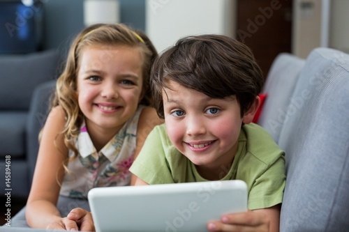 Portrait of siblings using digital tablet in living room