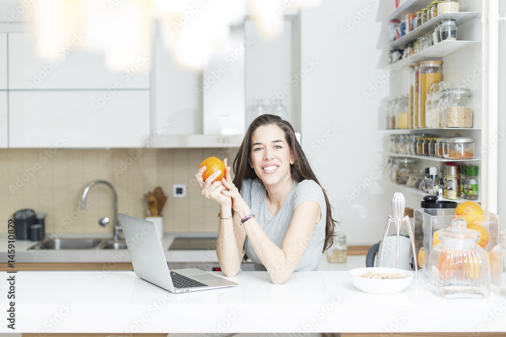 Morning scene. Beautiful woman holding orange in front of laptop Morning scene. Beautiful woman holding orange in front of laptop
