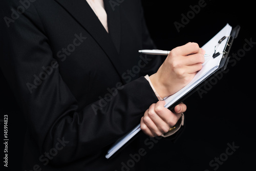 partial view of businesswoman writing in notepad isolated on black