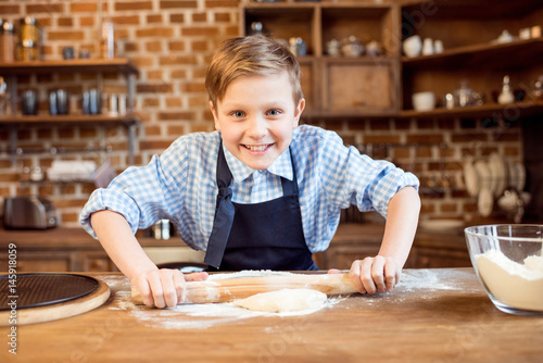 little boy making pizza dough on wooden tabletop in kitchen