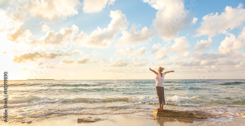 Relaxed woman enjoying sun, freedom and life an beautiful beach in sunset. Young lady feeling free, relaxed and happy. Concept of vacations, freedom, happiness, enjoyment and well being. photo