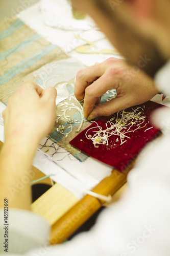 Detail of a man's hands embroiderer with a sewing thread gold on fabric.