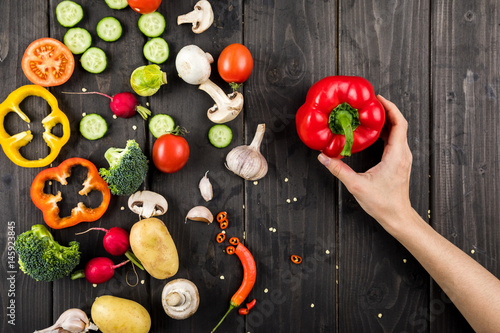 Top view of hand holding pepper and fresh vegetables on wooden table background