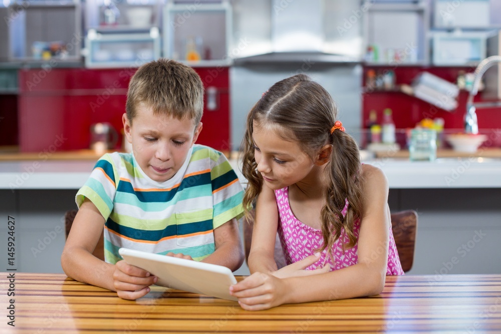 Siblings using digital tablet in kitchen Siblings using digital tablet in kitchen