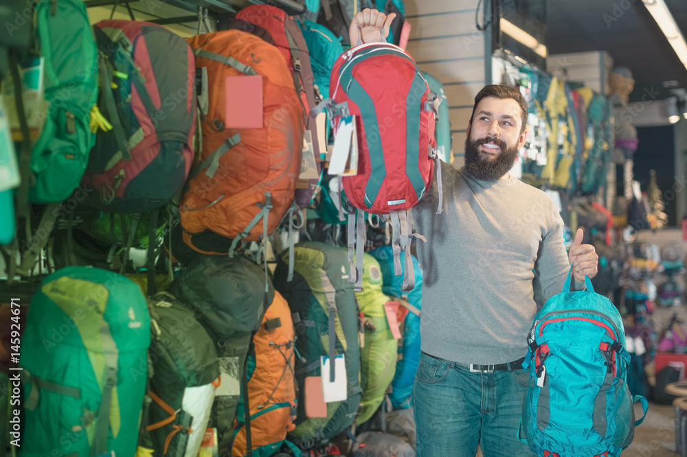 Young man customer examining backpacks in store