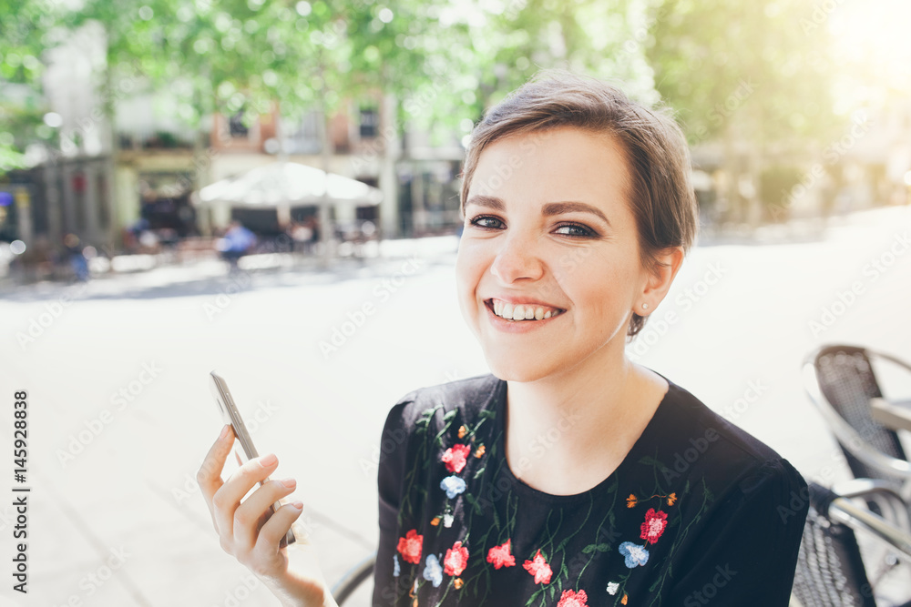 Close-up portrait of attractive young Caucasian woman talking on mobile phone at outdoor cafe. Girl talking by mobile phone, smiling. Sunny day. Outdoor photo. Close-up portrait of attractive young Caucasian woman talking on mobile phone at outdoor cafe. Girl talking by mobile phone, smiling. Sunny day. Outdoor photo.