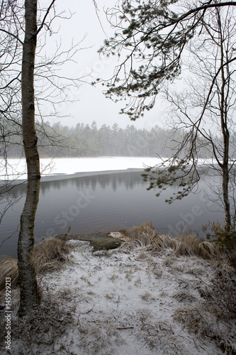 Lake side view on a spring morning. Snow blizzard and reflecting waters. Snow storm hit the morning.
