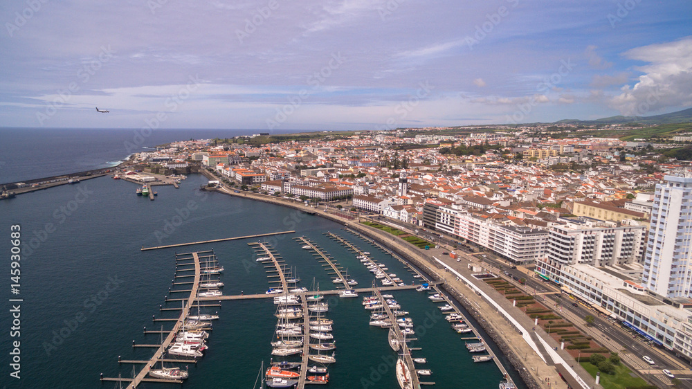 Fototapeta premium A view on Ponta Delgada from marina, Sao Miguel, Azores, Portugal. Moored yachts and boats along the port piers on a beautiful morning.