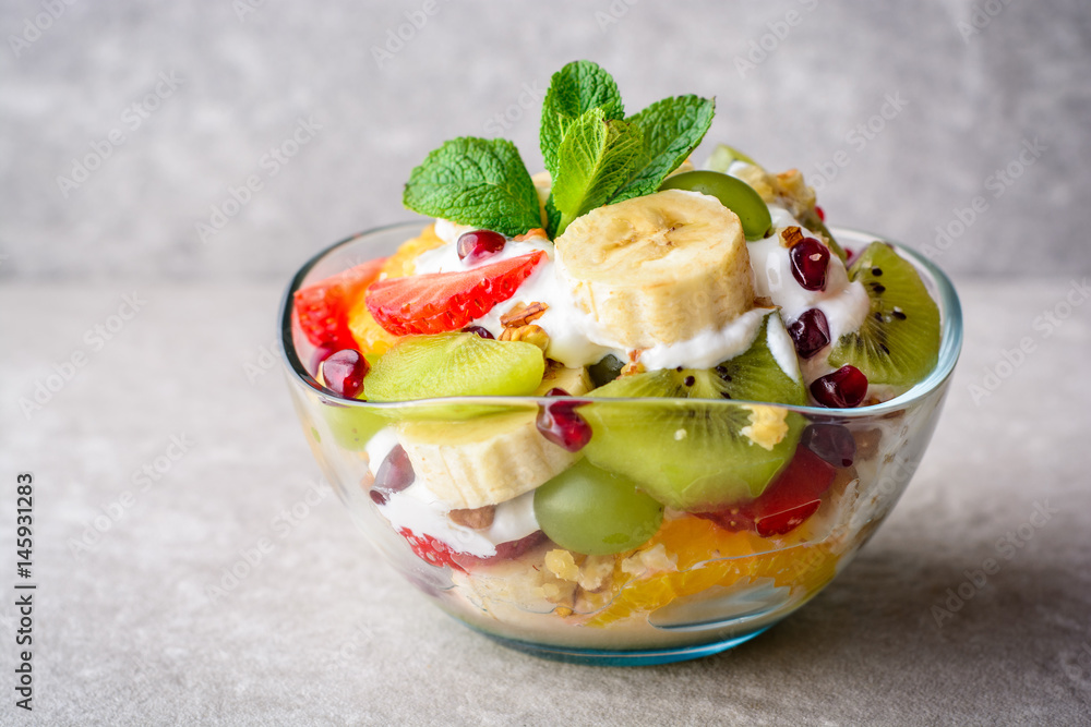 Fresh fruit salad with yogurt and walnuts in glass bowl on stone background. Fresh fruit salad with yogurt and walnuts in glass bowl on stone background.