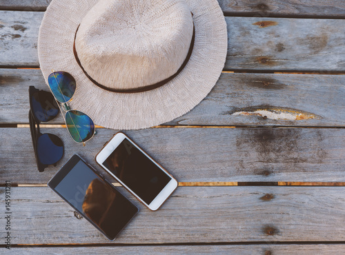 Straw hat, smart phone and sunglasses on wood bridge at tropical beach.