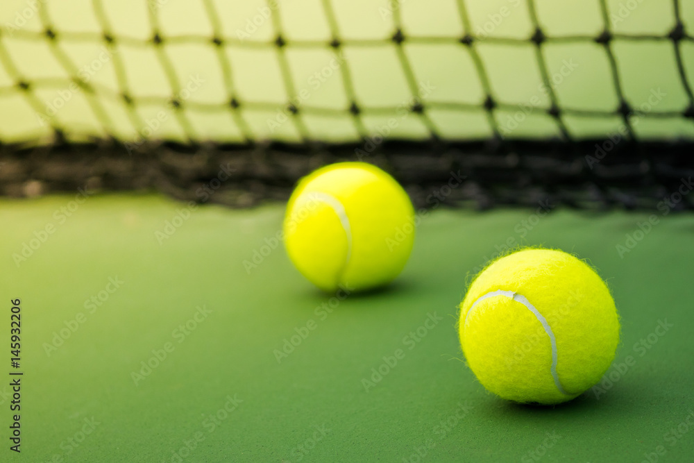 two tennis balls on green court, black weaved net as background, focus on one of two balls