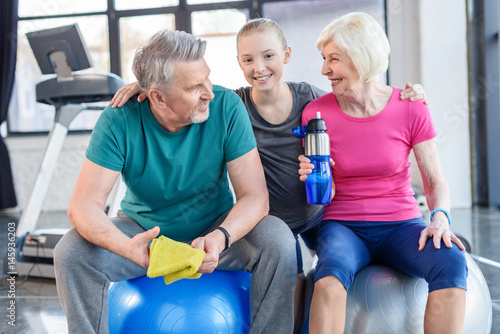 Smiling senior couple sitting on fitness balls and smiling girl in fitness class