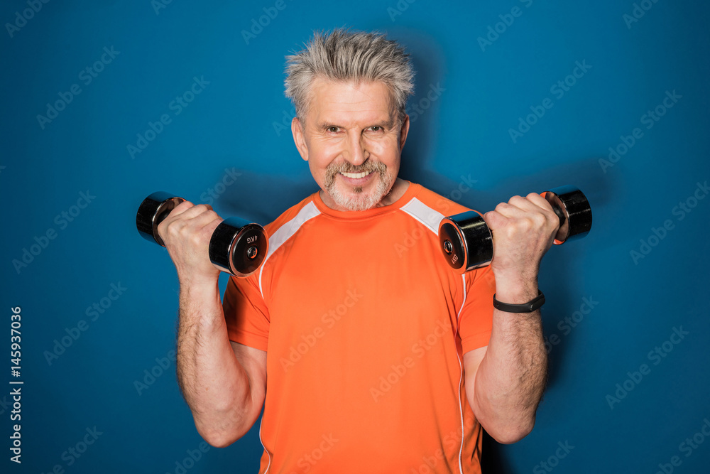 Smiling mature sportsman exercising with dumbbells and looking at camera Smiling mature sportsman exercising with dumbbells and looking at camera