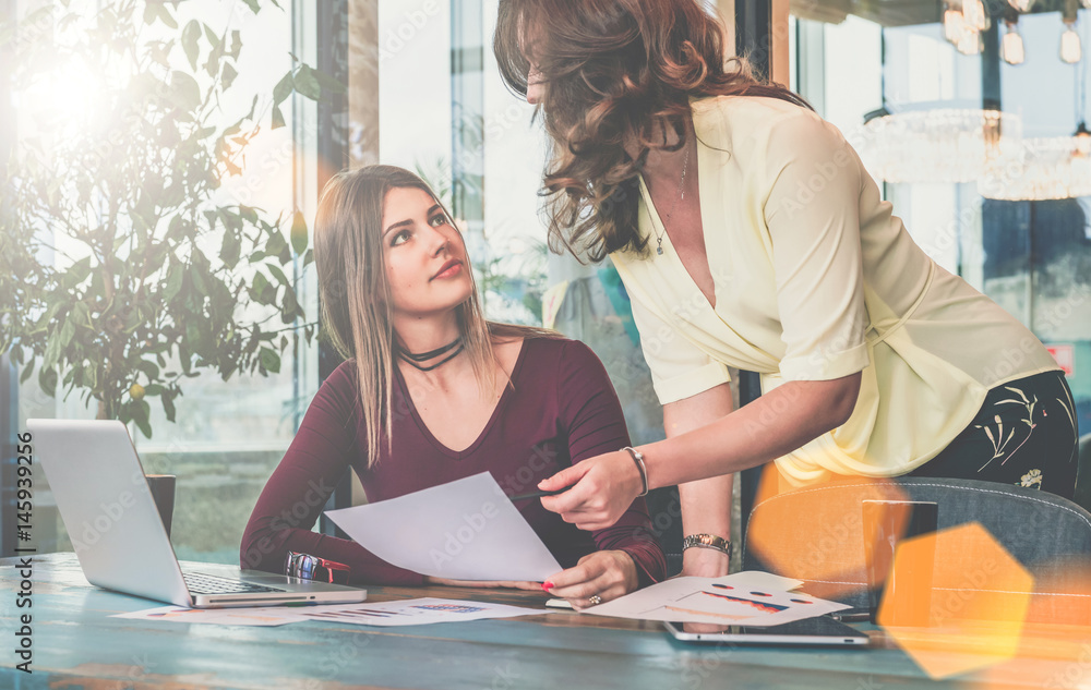 Obraz premium Two young businesswomen are discussing business plan.Girl holding documents.