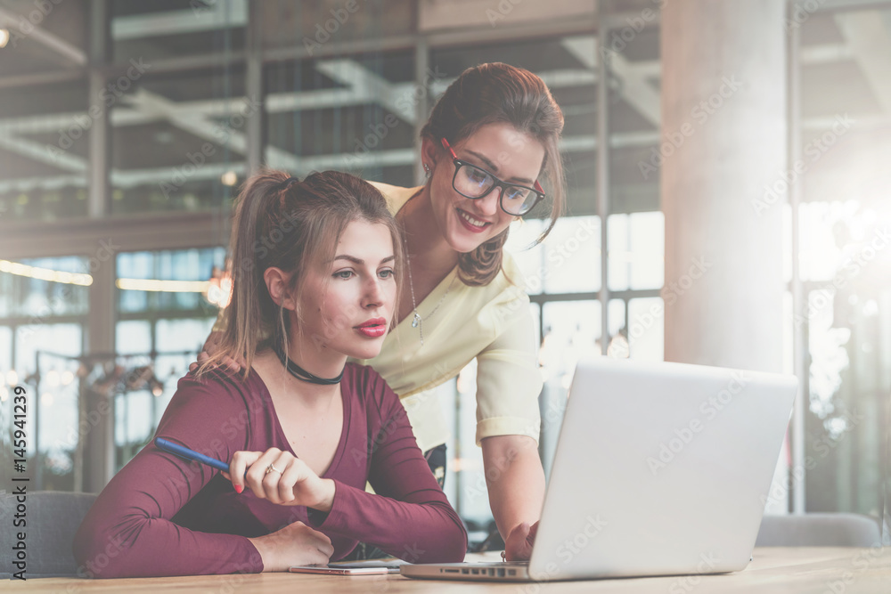 Teamwork. Two young businesswomen are working in office. Woman in glasses typing on laptop, second looks at screen. Teamwork. Two young businesswomen are working in office. Woman in glasses typing on laptop, second looks at screen.