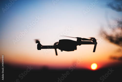 Flying drone into the sunset. Silhouette against sun. Quad copter in motion.