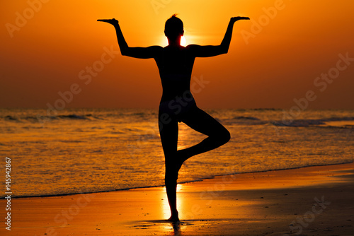 Kobieta ćwicząca jogę na plaży przy zachodzie słońca