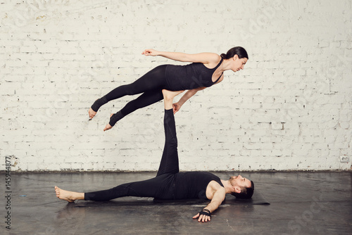 Young athletic couple practicing acroyoga. Balancing in pair. Fit active pair yoga time. Sporty handsome man supporting and holding slim beautiful brunette woman. Training time. Asana 