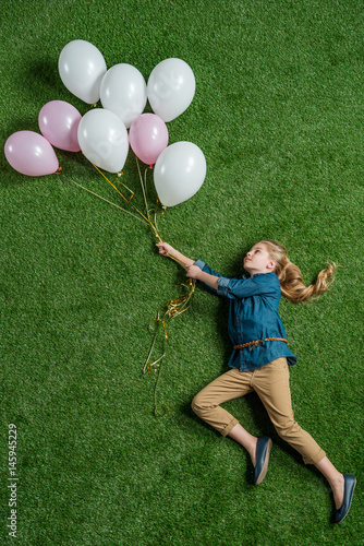 top view of little girl holding balloons on green grass