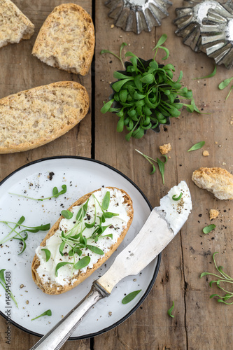 Obraz na płótnie Brötchen mit Frischkäse, Kresse und Pfeffer zusammen mit einem Teller und einem Messer auf einem alten rustikalen Holzuntergrund w salonie