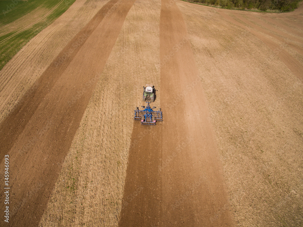 aerial view of a tractor at work - tractor plough cultivating beautiful fields  - agricultural machinery
