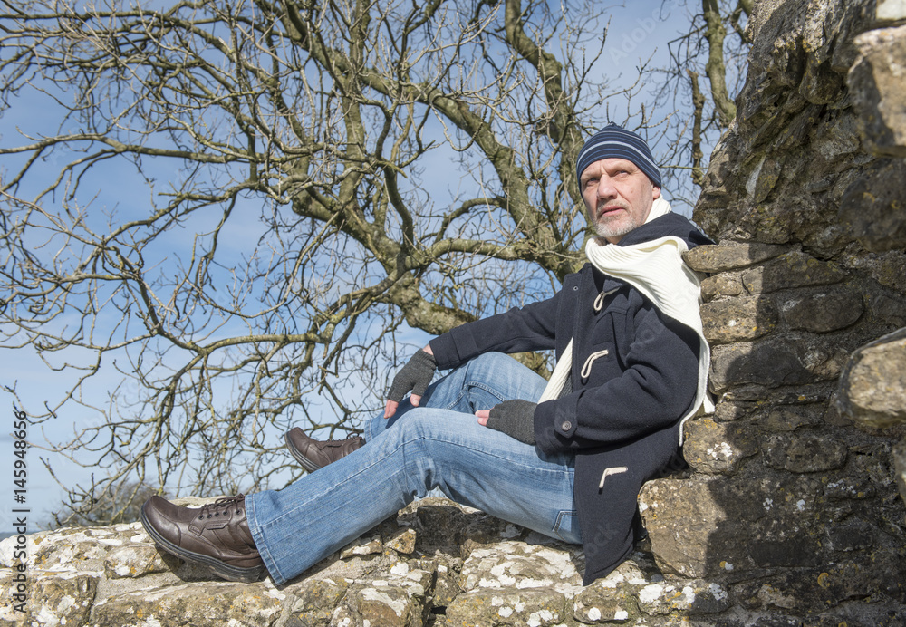 Fototapeta premium Mature man sitting on a stone wall in winter 