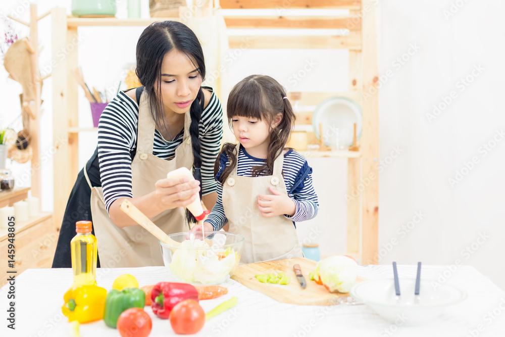 A little girl learning cooking practice with her Mom on salad bowl in kitchen background
