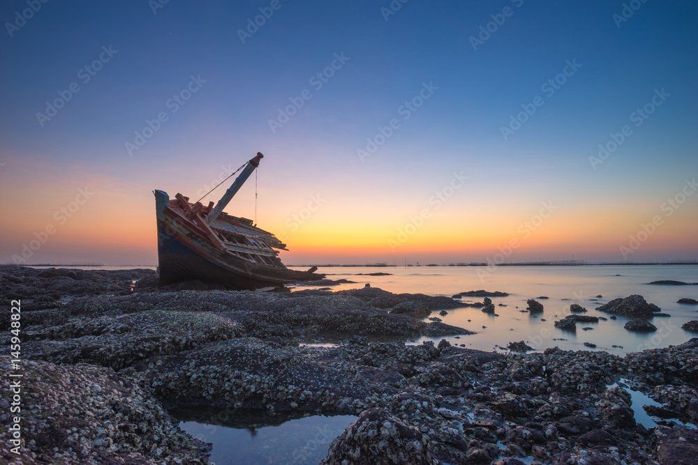 Fishing boat aground on the rocks for a long time at sea erosion disintegrated until only half a body which remains beautiful during twilight.