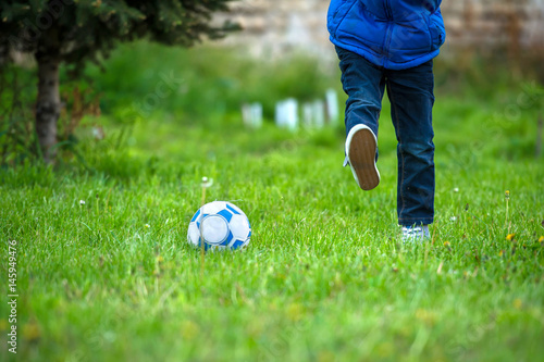 child boy playing football, shooting ball outdoor on grass