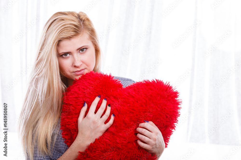 Sad woman holding red pillow in heart shape Sad woman holding red pillow in heart shape
