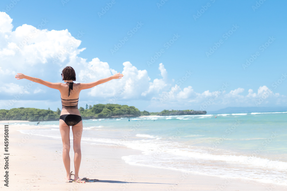 Freedom concept. Freedom and happiness woman on the tropical beach of Bali island, Indonesia. She is enjoying serene ocean nature during travel holidays vacation outdoors.