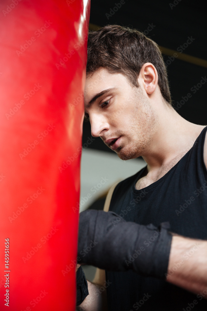 Tired man boxer leaning on punchbag