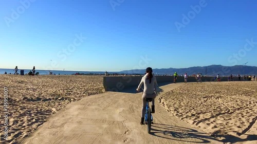 Junge Frau beim Fahhradfahren am Strand von Santa Monica und Venice Beach in Los Angeles, Kalifornien, USA