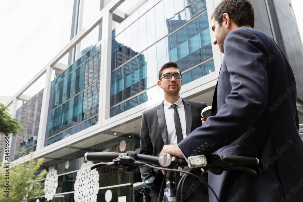 Two young businessmen with a bike in city centre Two young businessmen with a bike in city centre