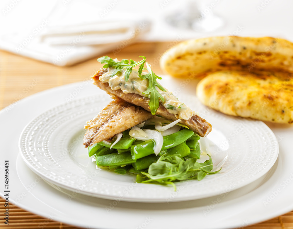 Smoked mackerel on a bed of green beans topped with sauce and rocket leaves. Smoked mackerel on a bed of green beans topped with sauce and rocket leaves.