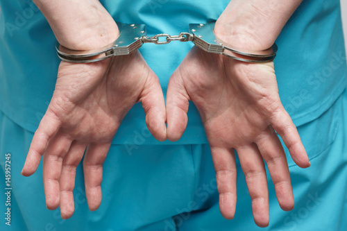 Obraz na plátně Yung doctor in blue uniform with stethoscope attached to handcuffed at the wrist
