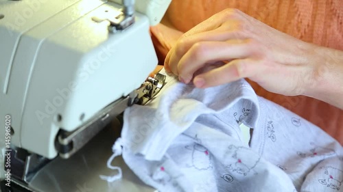 Closeup of adult female hands of seamstress at work. Woman sewing clothes for newborn babies with professional machine in factory. Real time full hd video footage. photo