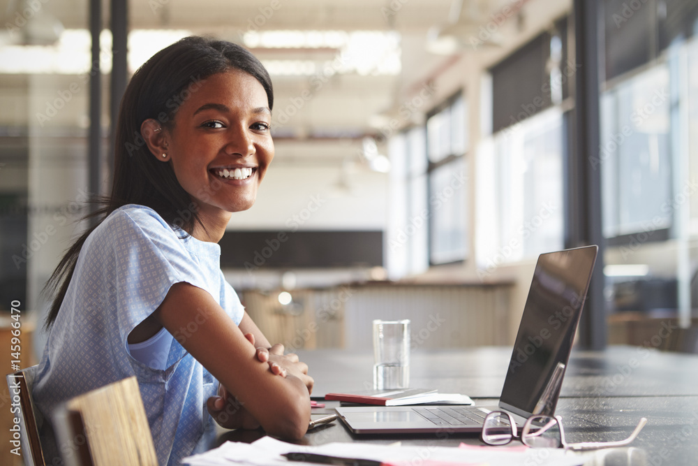 Fototapeta premium Young black woman in office using laptop smiling to camera