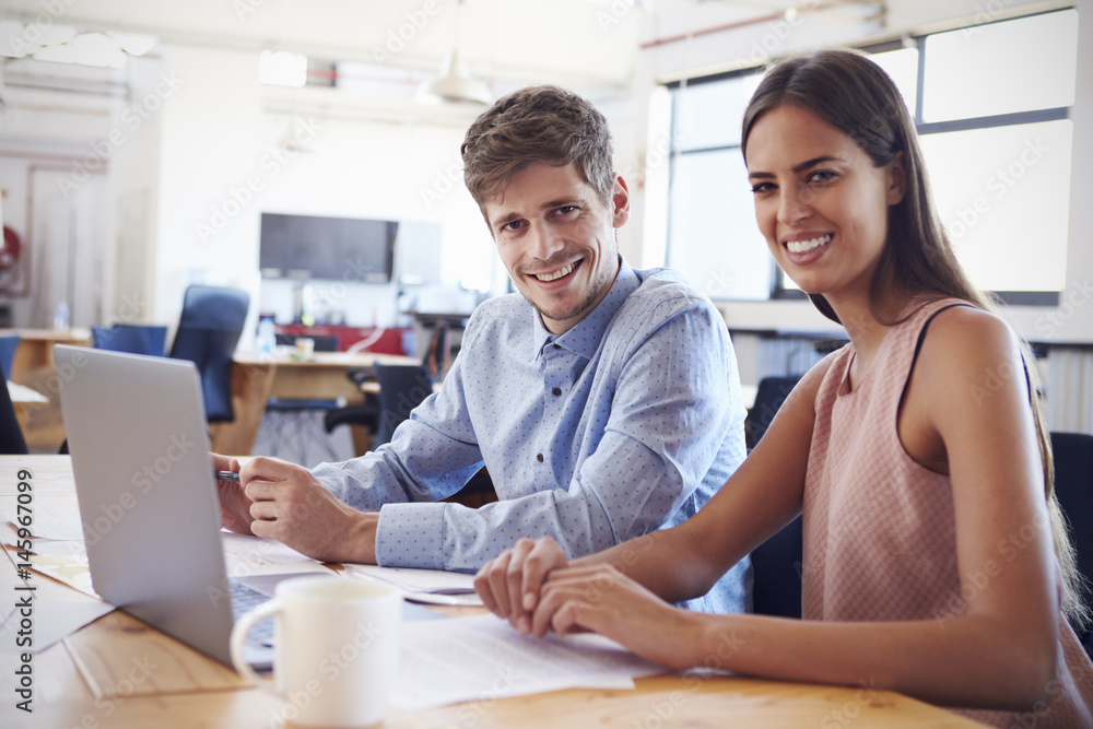 Young man and woman working in office smiling to camera Young man and woman working in office smiling to camera
