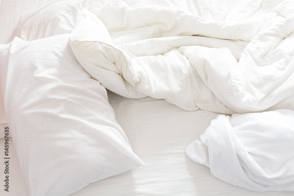Top view of an unmade bed after waking up in the morning. White pillows, a blanket and a shower towel are on the bed. Top view of an unmade bed after waking up in the morning. White pillows, a blanket and a shower towel are on the bed.